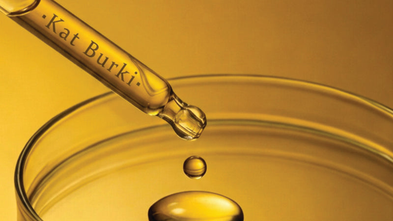 Kat Burki serum dropper releasing a golden drop of copper peptide serum